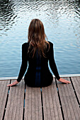 Woman Sitting on Pier at Edge of Lake, Rear View