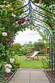 A garden with a rose arch, and a deck chair.