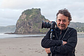 blocked for illustrated books in Germany, Austria, Switzerland: Photographer Karl Johaentges with camera on Piha beach, North Island, New Zealand