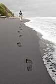 Schwarzer Sandstrand, Fußspuren im schwarzer Sand, Frau geht am Strand, Südinsel, Neuseeland
