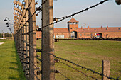 View of the Main Guard House through the electrified barbed wire fence separating sections of the Auschwitz-Birkenau Concentration Camp, Oswiecim, Malopolska, Poland