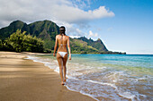 Hawaii, Kauai, Haena Beach Tunnels Beach, Woman walking along sandy shore.