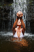 Hawaii, Oahu, Manoa Falls, Beautiful female sitting at the bottom of Manoa Waterfall, cupping water above her.