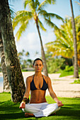 Hawaii, Woman meditating on grass near beach.