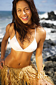 Hawaii, Oahu, Attractive woman wearing grass skirt on a rocky ocean shore.