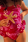Close-up girl pink bathing suit holding starfish in front, hand on hip D1062