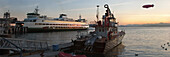 A sunset view over a harbour.  Elliott Bay in Puget Sound, on the Washington coastline. An airship in the sky, above a fishing boat and a cruise ship., Shipping and zeppelin