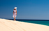 Young woman with hat walking along a sand dune, Playa de Sotavento, Sotavento, Costa Calma, Jandia, Morro jable, Fuerteventura, Canary Islands, Spain, Europe