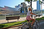 Woman riding a bicycle near Guggenheim museum, Bilbao, Basque Country, Spain