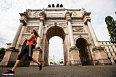 Female jogger passing Siegestor (vitory gate), Munich, Bavaria, Germany