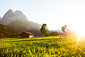 Mountainbiker fährt an Wiesen mit Heustadel vorbei, Grainau, Bayern, Deutschland