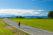 Joggerin läuft über Landstraße, Münsing, Bayern, Deutschland