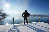 Mann steht auf einem verschneiten Steg am Kochelsee, Oberbayern, Deutschland