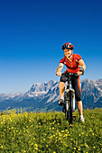 Female mountain biker on Planai, Dachstein mountains in background, Schladminger Tauern, Styria, Austria