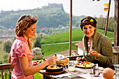 Zwei junge Frauen beim Essen, Burg Riegersburg im Hintergrund, Riegersburg, Steiermark, Österreich