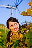 Young woman between grapevines, klopotec in background, Styria, Austria