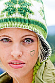 Junge Frau mit Mütze und Herzen auf der Wange, Steiermark, Österreich