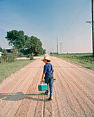 USA, Minessota, rear view of a young Amish boy walking on dirt road and carrying cooler
