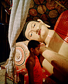 'SRI LANKA; Asia; young monk standing by Buddha statue'