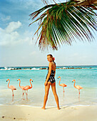 ARUBA, portrait of young woman standing on the beach smiling in the middle of Pink Flamingos, Renaissance Island