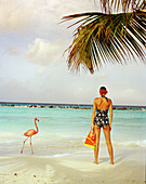 ARUBA, portrait of young woman standing on the beach in the middle of Pink Flamingos, Renaissance Island