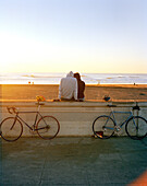 USA, San Francisco, a couple sit and watch the sunset at Ocean Beach