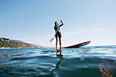 USA, California, Malibu, El Pescador Beach, an athletic woman paddles her paddleboard along the Malibu coast