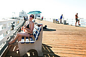USA, California, Malibu, Abigail enjoys the sun and fixes her bikini on the Malibu Pier, Surfrider Beach