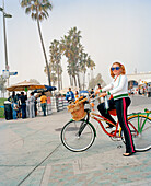 USA, California, Los Angeles, Venice Beach, a hip young woman strikes a pose with her bike on the Venice Beach Boardwalk