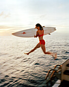 FIJI, Northern Lau Islands, a woman jumps off of a yacht with her surfboard, Southern Pacific Ocean