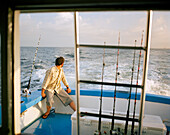 USA, Florida, man sitting on fishing boat heading out to sea, Destin
