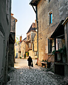 FRANCE, Burgundy, senior woman walking on pathway by buildings, rear view, Noyers