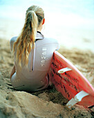 USA, Hawaii, Oahu, a young woman surfer sits on the beach and watches the waves at Pipeline, The North Shore