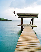 HONDURAS, Roatan, boy jumping off pier to get his soccer ball
