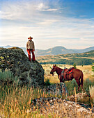USA, Montana, cowboy standing on rocks holding horse lead rope, Gallatin National Forest, Emigrant
