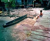 PANAMA, Bocas del Toro, Salt Creek Islands, Guaymi Indian boy sits on a dock by a dugout canoe, Central America