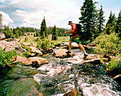 USA, Wyoming, man with backpack crossing stream, Yellowstone National Park