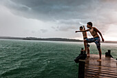 Two young men on a jetty leaning into the wind, Lake Starnberg, Bavaria, Germany