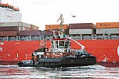 Tractor tugboat in front of a container ship, Altenwerder, Hamburg, Germany