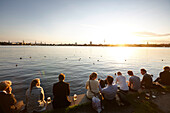 People sitting on a seawall at Alsterperle cafe and bar, Eduard-Rhein-Ufer 1, Outer Alster Lake, Hamburg, Germany