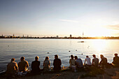 People sitting on a seawall at Alsterperle cafe and bar, Eduard-Rhein-Ufer 1, Outer Alster Lake, Hamburg, Germany