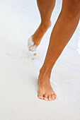 Woman’s running feet in white sand