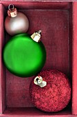 Three green, red and gold Christmas baubles close up in a red wooden box.
