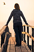 Woman on wooden pier at sunrise, seagull silhouette in distance, Lake Winnipeg, Matlock, Manitoba