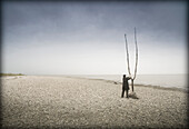 Man in Hat and Coat Standing on Beach Adjusting Large Branch, Winnipeg, Manitoba