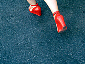 Close up of the woman feet wearing red shoes and walking in the street