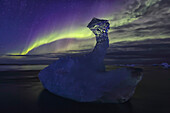 Aurora borealis dances over iceberg from the glacial lagoon jokulsarlon, iceland