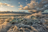 Waves from the atlantic ocean crashes over icebergs along the coast at sunrise, iceland