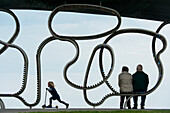 Girl On Scooter Going Past Old Couple Sitting On 'the Longest Bench' , Littlehampton, West Sussex, Uk