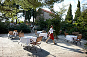 Waiter and coffee tables on the Piazza under trees, Aman Sveti Stefan, Sveti Stefan, Montenegro
